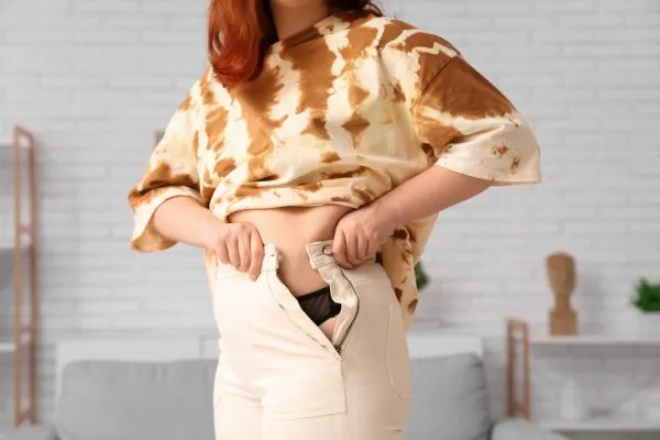 Image of woman trying to do her trousers up after pregnancy weight gain Winkfield