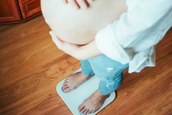 Image of woman weighing herself and experiencing weight gain through pregnancy Winkfield